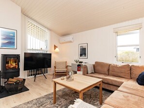 A living room with a fireplace, a television, a sofa, a coffee table, and a patterned rug. - 4 Star Holiday Home in Lokken (Lokken)