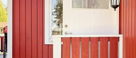 Une porte en bois rouge, avec une fenêtre blanche et un luminaire noir fixé au mur.