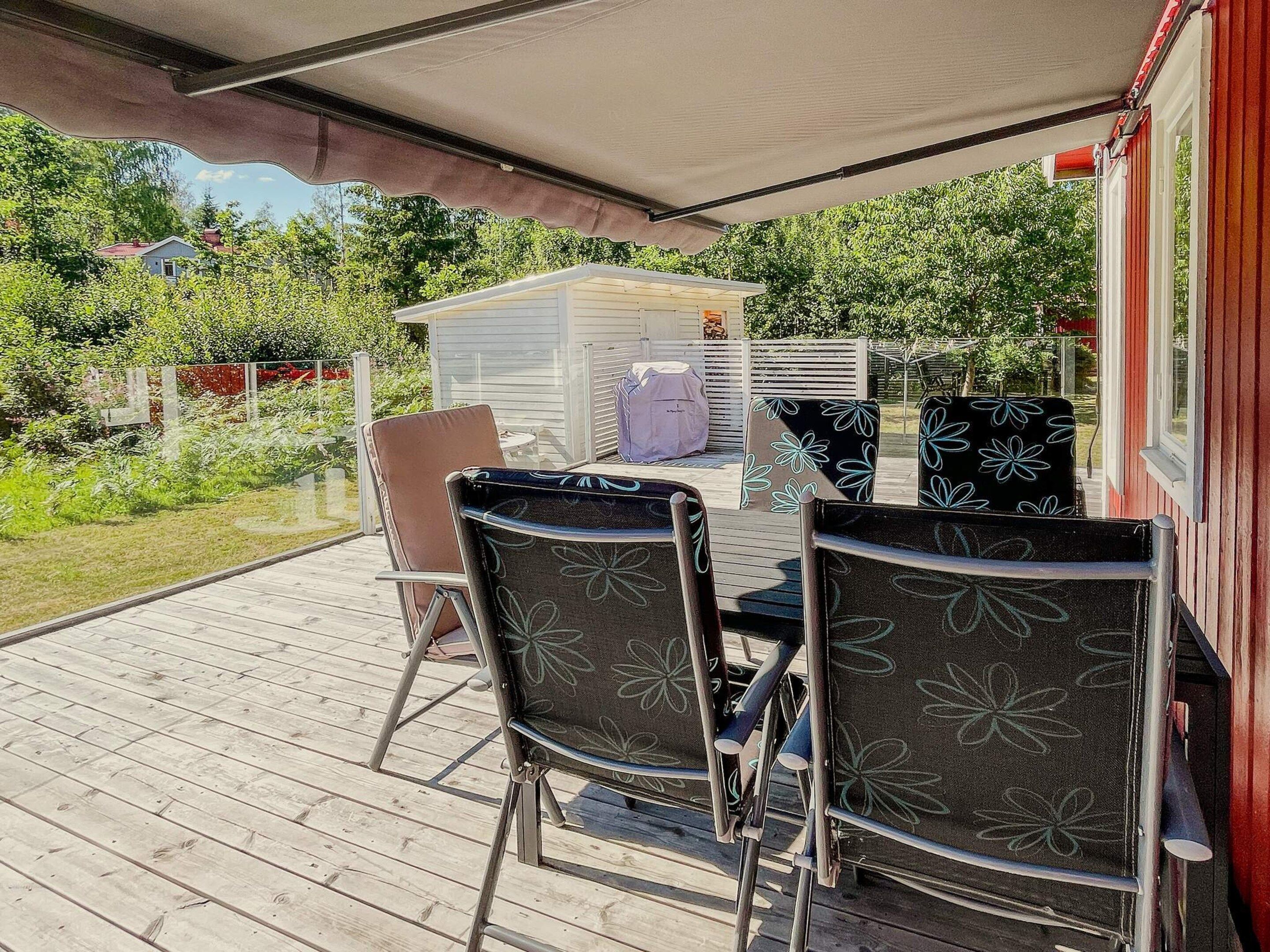 Une terrasse extérieure avec une table et des chaises, un espace abrité et une vue sur une maison et de la verdure.