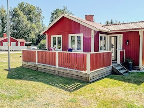 A red cabin with a porch, a chimney, and a small set of stairs leading to the entrance.