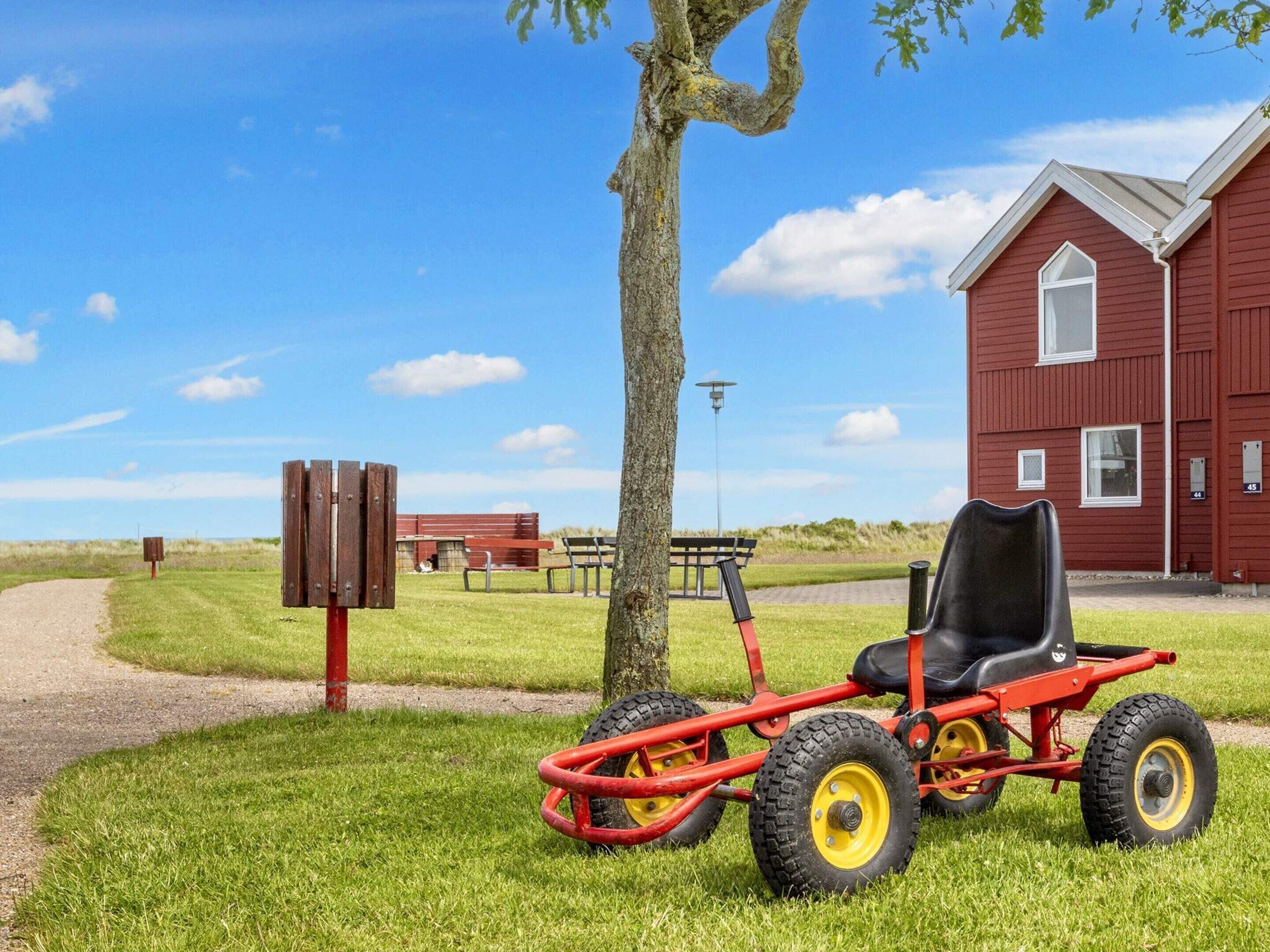 A red building with a window, a tree, and a red lawnmower.