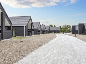 Eine Reihe moderner, dunkel gefärbter Hütten mit Satteldächern, die an einem Schotterweg entlang verlaufen.