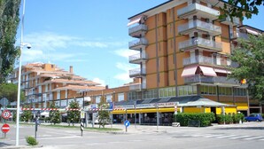 Un edificio de varios pisos con balcones, un restaurante con toldos amarillos y un cielo azul despejado.