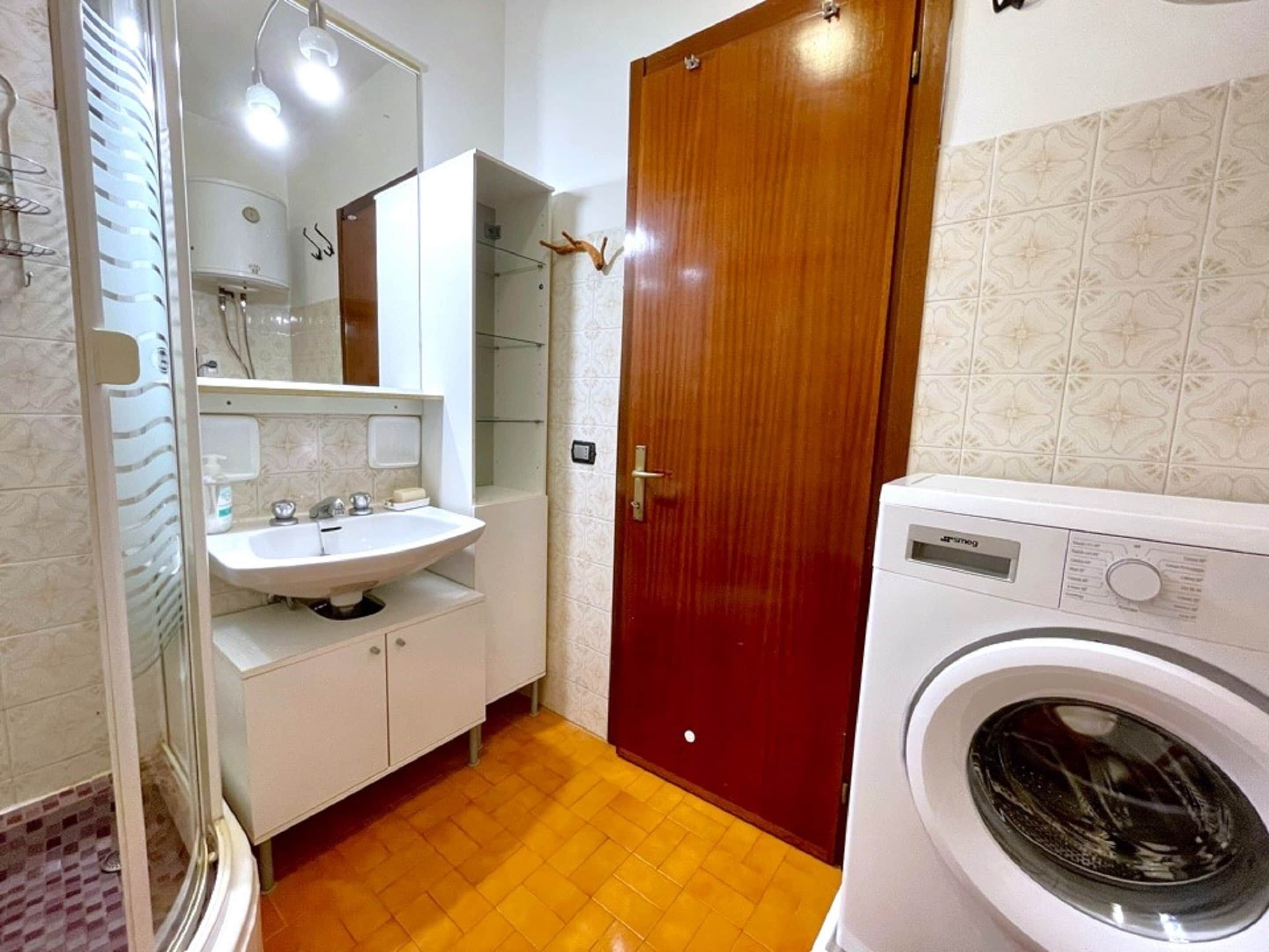 Ein Badezimmer mit Waschbecken, Spiegel, Holztür und Waschmaschine.