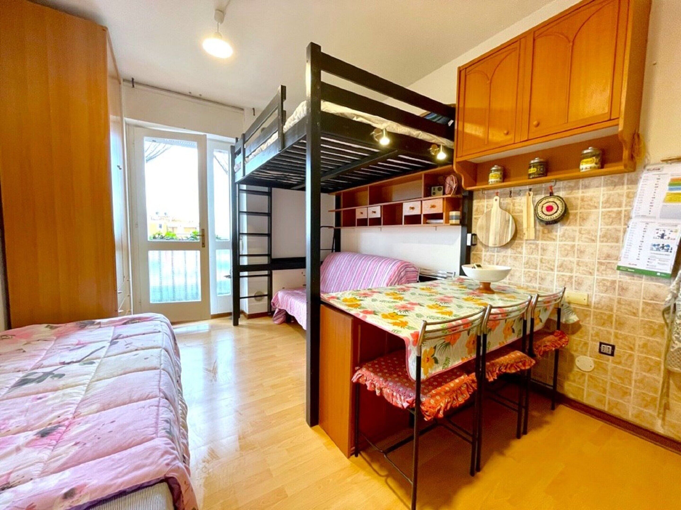 A compact room with a bunk bed, a small kitchen area with a table and chairs, and a window providing natural light.