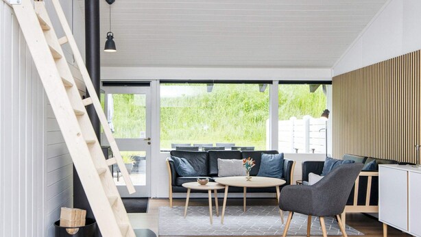 Ein modernes Wohnzimmer mit Holzboden, einer Couch, einem Sessel, einem kleinen Tisch und einer an der Wand angelehnten Leiter.