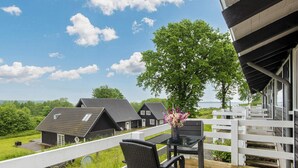 Eine Holzterrasse mit Tisch und Stühlen, mit Blick auf eine Häuserreihe und ein Gewässer.