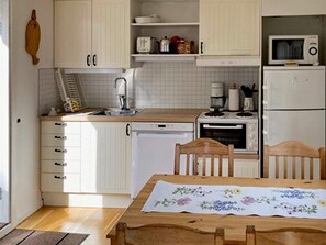 A kitchen with white cabinets, a wooden table with a floral tablecloth, and a microwave on the countertop.