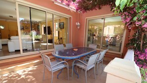 Une terrasse avec une table ronde et des chaises, de grandes portes-fenêtres coulissantes et une vue sur l’intérieur.