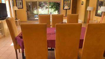 Un coin repas avec une table dressée pour six personnes, entourée de chaises, dans une pièce aux murs jaunes et dotée d’une grande fenêtre.