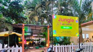 Een hostel genaamd Jungle by Sturmfrei, met een naambord, geparkeerde scooters en een eetgedeelte met terras.