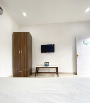 Een kamer met een houten garderobe, een witte tafel met een blauwe vaas, en een tv aan de muur.
