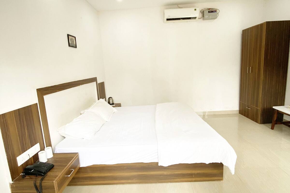 A bedroom with a wooden bed, a nightstand with a phone, a ceiling fan, and an air conditioning unit.
