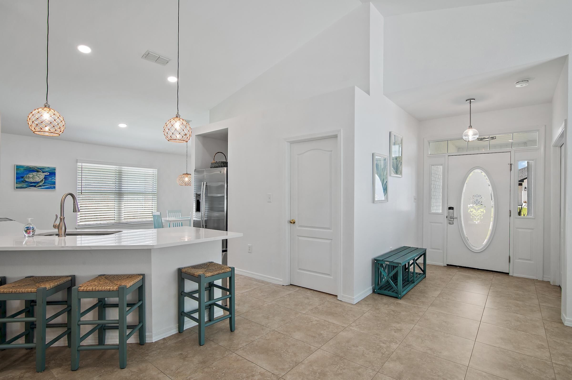 A modern kitchen with a white island, bar stools, pendant lights, and a refrigerator.