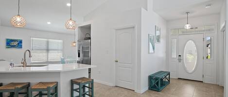 A modern kitchen with a white island, bar stools, pendant lights, and a refrigerator.