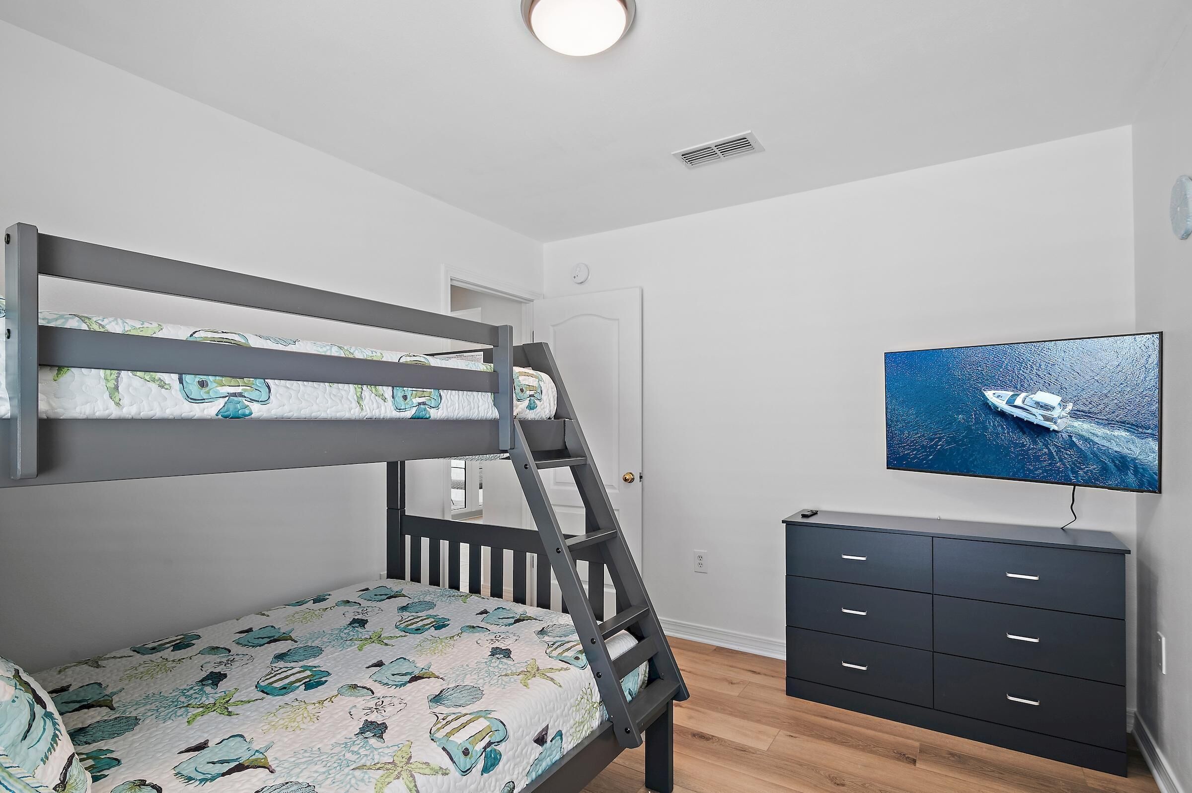 A bunk bed with a ladder, a television on the wall, and a dresser.