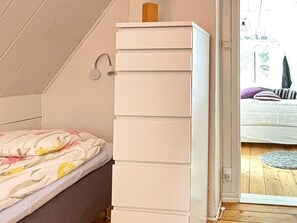 A bedroom with a bed, a white dresser, and a view of an outdoor area.