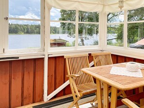 Un espace extérieur aménagé avec des meubles en bois, une table et des chaises, protégé par un auvent et offrant une vue sur un lac et une forêt.
