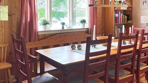 Une table de salle à manger en bois, des chaises, une bibliothèque et une fenêtre avec des rideaux.