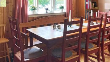 A wooden dining table with chairs, a bookshelf, and a window with curtains.