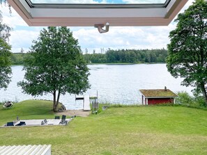 A lakeside view with a red cabin, a large tree, and a grassy area with outdoor seating.