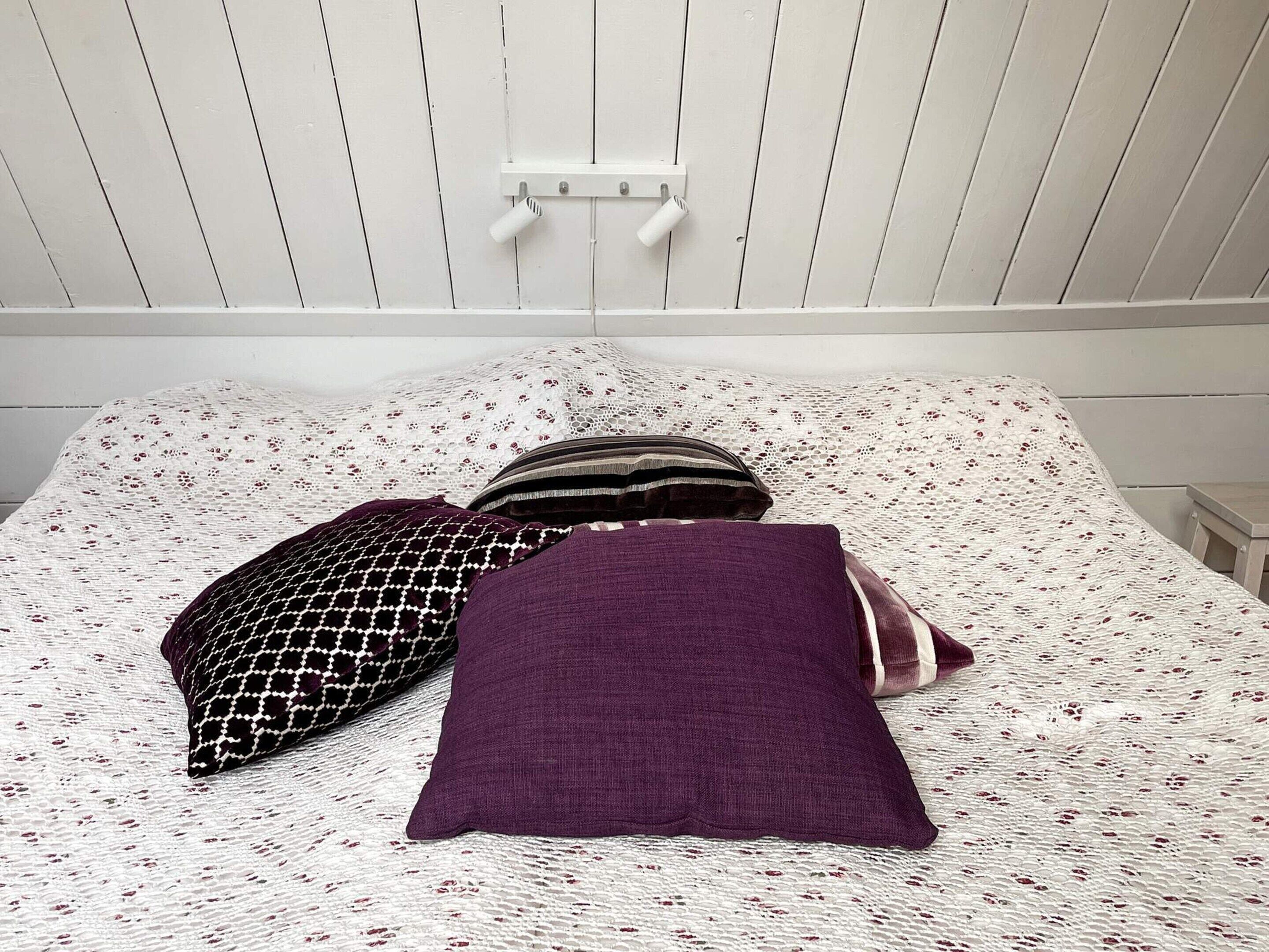 A bed with a patterned bedspread and multiple pillows, including a purple one.