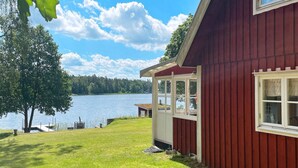 Ein rotes Holzhaus mit Glastür und -fenstern mit Blick auf einen See.