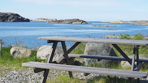 A wooden picnic table with benches overlooking a calm body of water and rocky outcrops. - 4 Star Holiday Home in Hamburgsund (Hamburgsund)