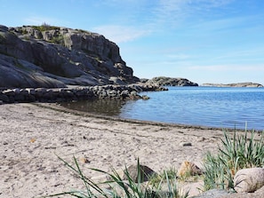 Un rivage rocheux bordé d’une eau calme, un ciel dégagé et une végétation clairsemée.
