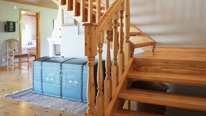 A wooden staircase leading to a landing with a blue trunk and a chair in a room with wooden flooring and a door in the background. - 4 Star Holiday Home in Hamburgsund (Hamburgsund)