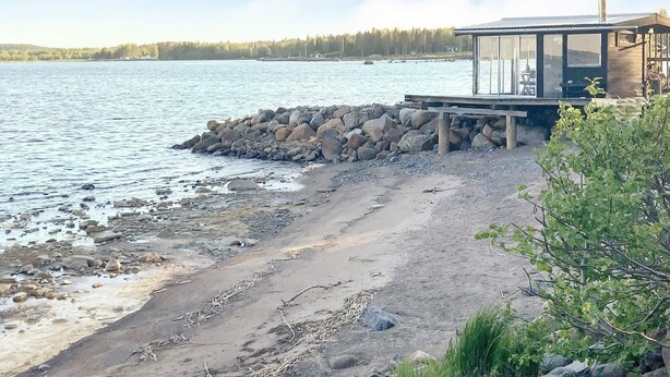 A beach with a wooden deck and a glass-enclosed structure, overlooking a calm body of water. - 4 Star Holiday Home in Lulea (Luleå)