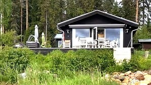 A cabin with a large window, surrounded by greenery and rocks. - 4 Star Holiday Home in Lulea (Luleå)