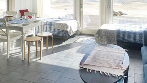 A room with a dining table, two chairs, a bed with patterned bedding, a small round table with a book, and a view of a frozen lake through large windows. - 4 Star Holiday Home in Lulea (Luleå)