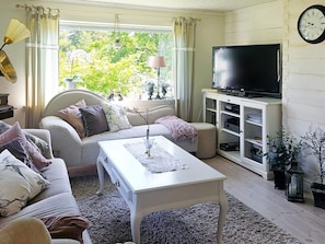 A living room with a sofa, a coffee table, a television on a cabinet, and a clock on the wall. - 4 Star Holiday Home in Myggenas (Myggenäs)