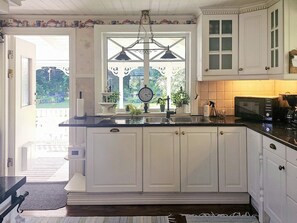 A kitchen with white cabinets, a black countertop, a window with a view of greenery, and a clock on the wall. - 4 Star Holiday Home in Myggenas (Myggenäs)