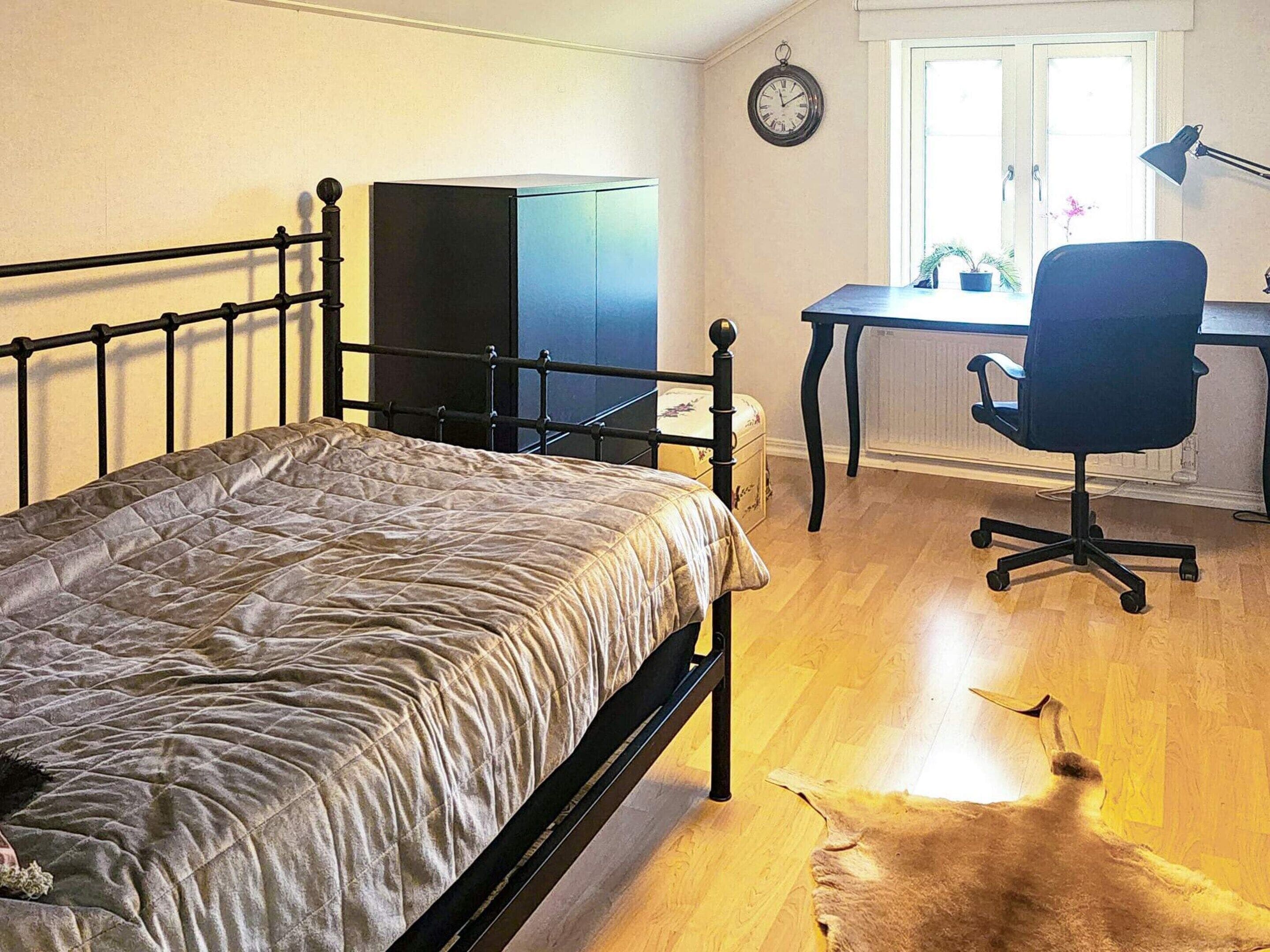 Une chambre à coucher avec un lit, un bureau, une chaise, une horloge et une fenêtre.