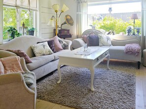 A cozy living room with a sofa, a coffee table, and a side table. There is a window with curtains, a lamp, and a plant. - 4 Star Holiday Home in Myggenas (Myggenäs)
