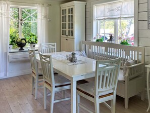 A dining area with a white table and chairs, a cabinet with glass doors, and a window with a view of greenery. - 4 Star Holiday Home in Myggenas (Myggenäs)