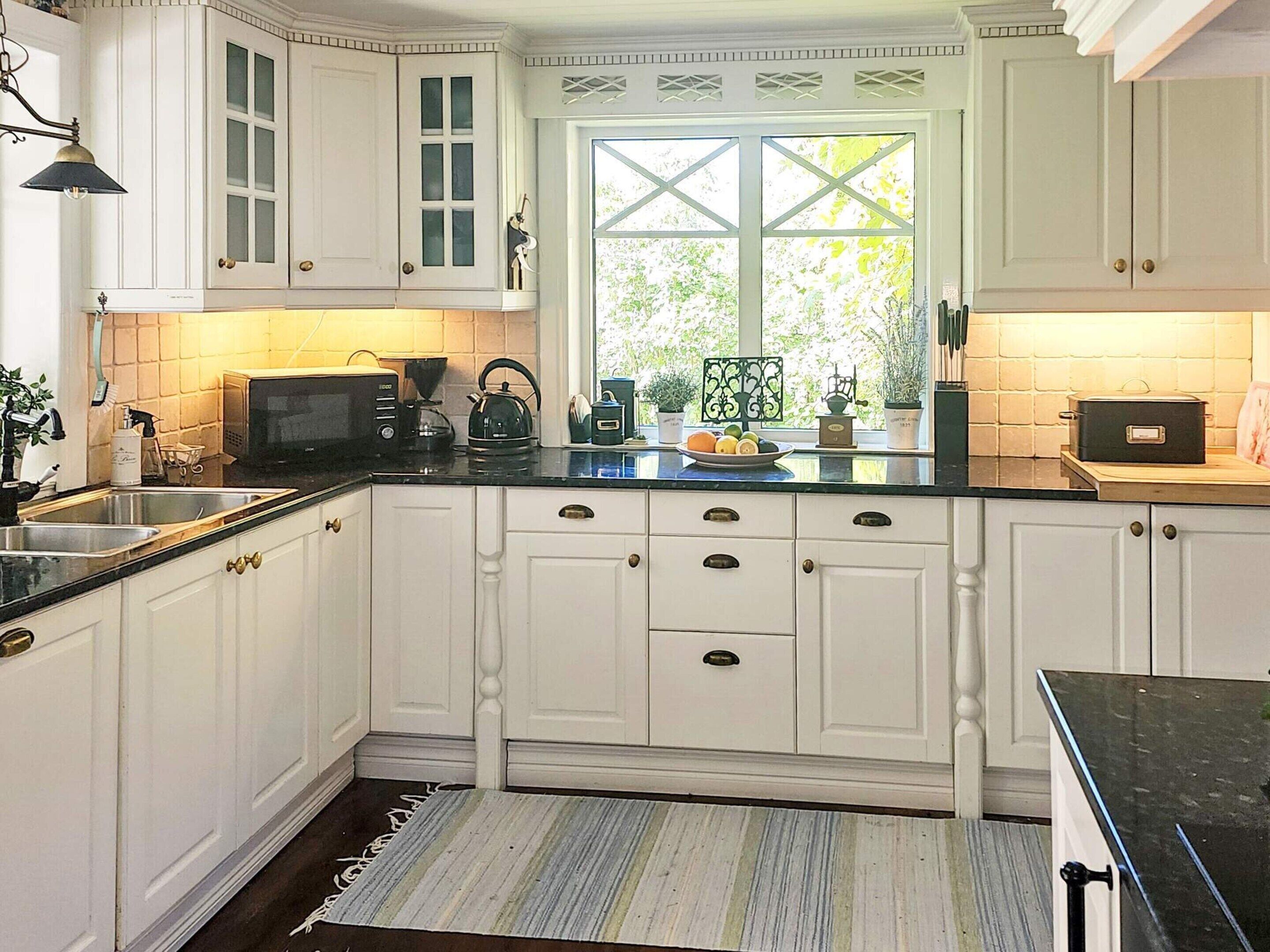 A kitchen with white cabinetry, a black countertop, and a window with a view of greenery.