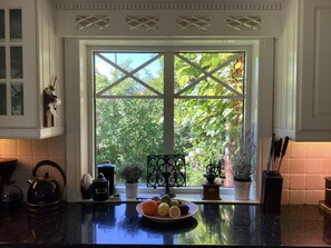 A kitchen with a large window, a tea kettle, a plate of fruit, and various kitchen utensils. - 4 Star Holiday Home in Myggenas (Myggenäs)