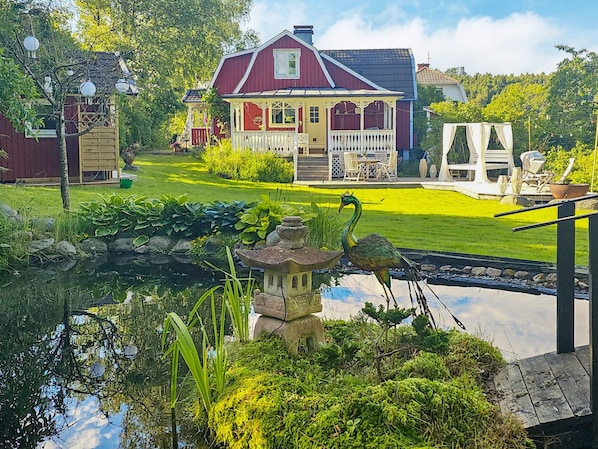 A house with a front porch, a small pond with a decorative stone structure, and a well-maintained lawn.