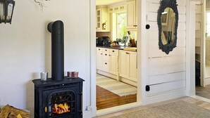 A room with a black wood-burning stove, a door leading to a kitchen with white cabinets, and a mirror on the wall. - 4 Star Holiday Home in Myggenas (Myggenäs)