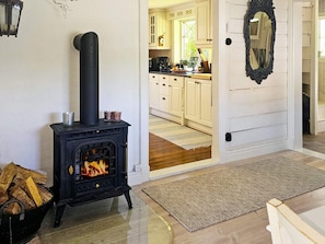 A room with a black wood-burning stove, a door leading to a kitchen with white cabinets, and a mirror on the wall. - 4 Star Holiday Home in Myggenas (Myggenäs)