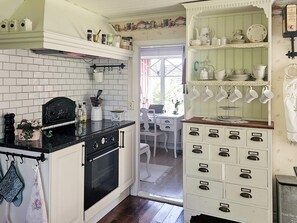 Et køkken med en sort bordplade, hvide skabe og en indbygget ovn. Der er et spiseområde at se gennem en åben dør.