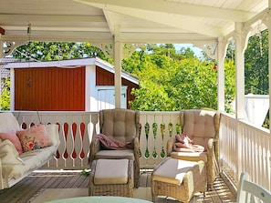 A covered outdoor seating area with wicker furniture and a white fence.