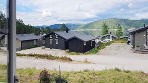 Blick auf ein Seeufergrundstück mit mehreren Holzhütten, einer Schotterauffahrt und einer Holzterrasse mit Pflanzen in Töpfen.