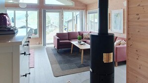 Ein gemütliches Zimmer mit großem Fenster, einer Couch, einem Tisch und einem Kaminofen.