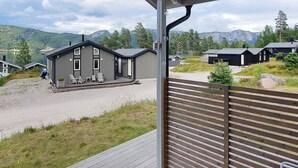 Eine moderne Holzhütte mit Terrasse, eingebettet in eine natürliche Landschaft mit Bergen und Bäumen.