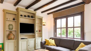A living room with a grey sofa, wooden beams, a TV on a cabinet, and a window with a view of greenery. - Holiday Home Nieuwpoort Near Sandy Beach (Nieuwpoort)