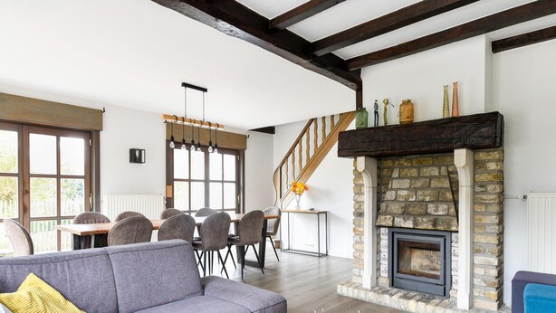 A modern living room with a grey sectional sofa, a round coffee table, a stone fireplace, and a wooden staircase. - Holiday Home Nieuwpoort Near Sandy Beach (Nieuwpoort)